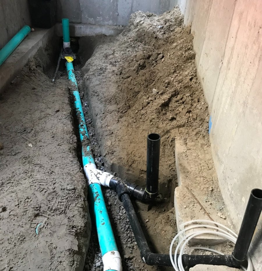 Indoor trench with newly installed green PVC and black ABS plumbing pipes for drainage and sewer connections in a residential basement construction site