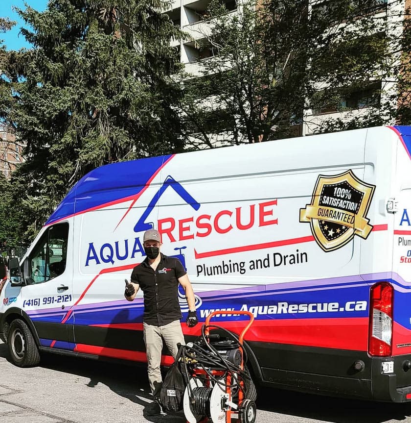 AquaRescue technician beside a branded plumbing van, with a drain-cleaning machine in front of the van.