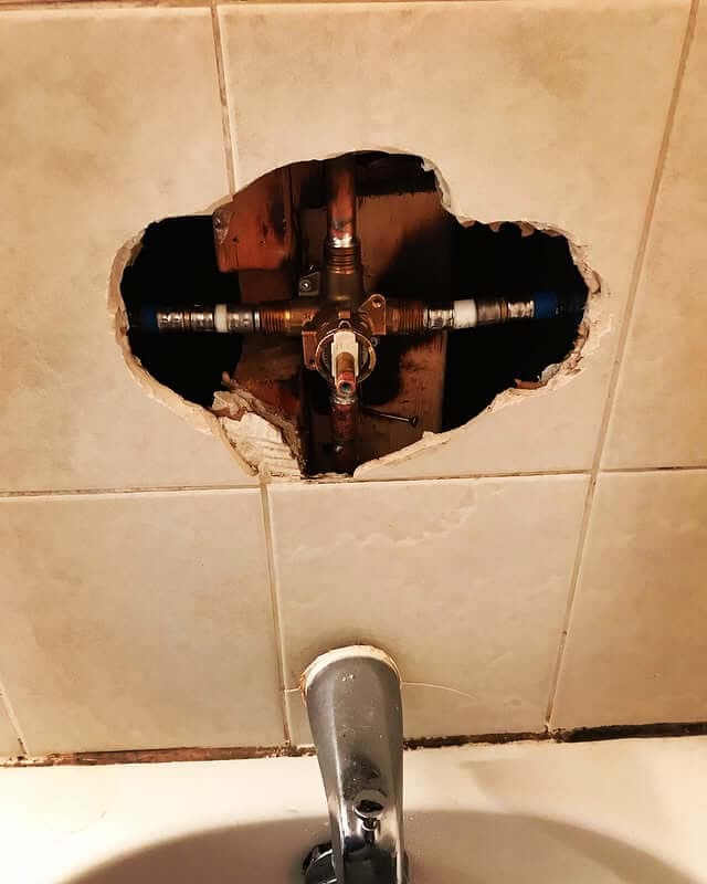 bathroom wall opened to access plumbing pipes