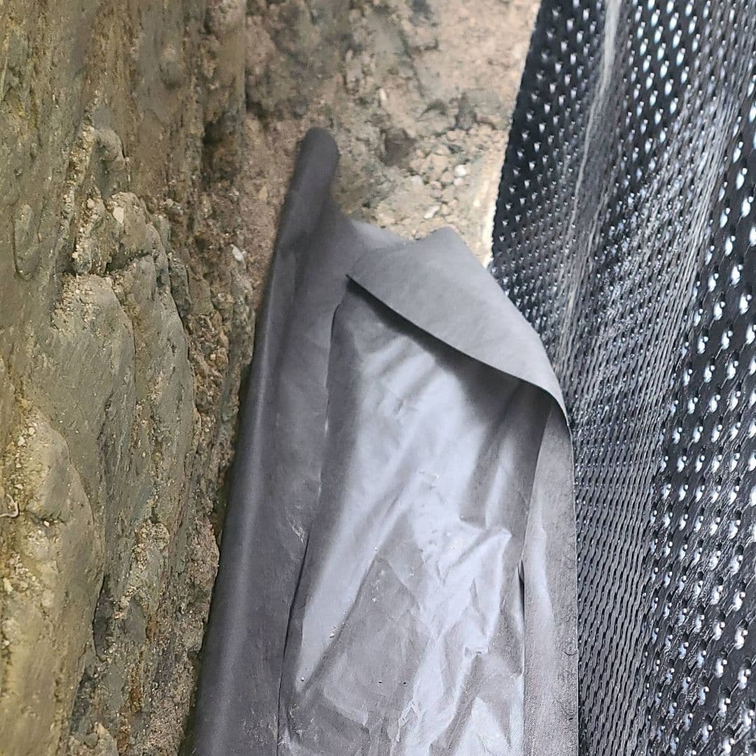 Foundation wall with waterproofing membrane and geotextile fabric in a trench for exterior drainage work