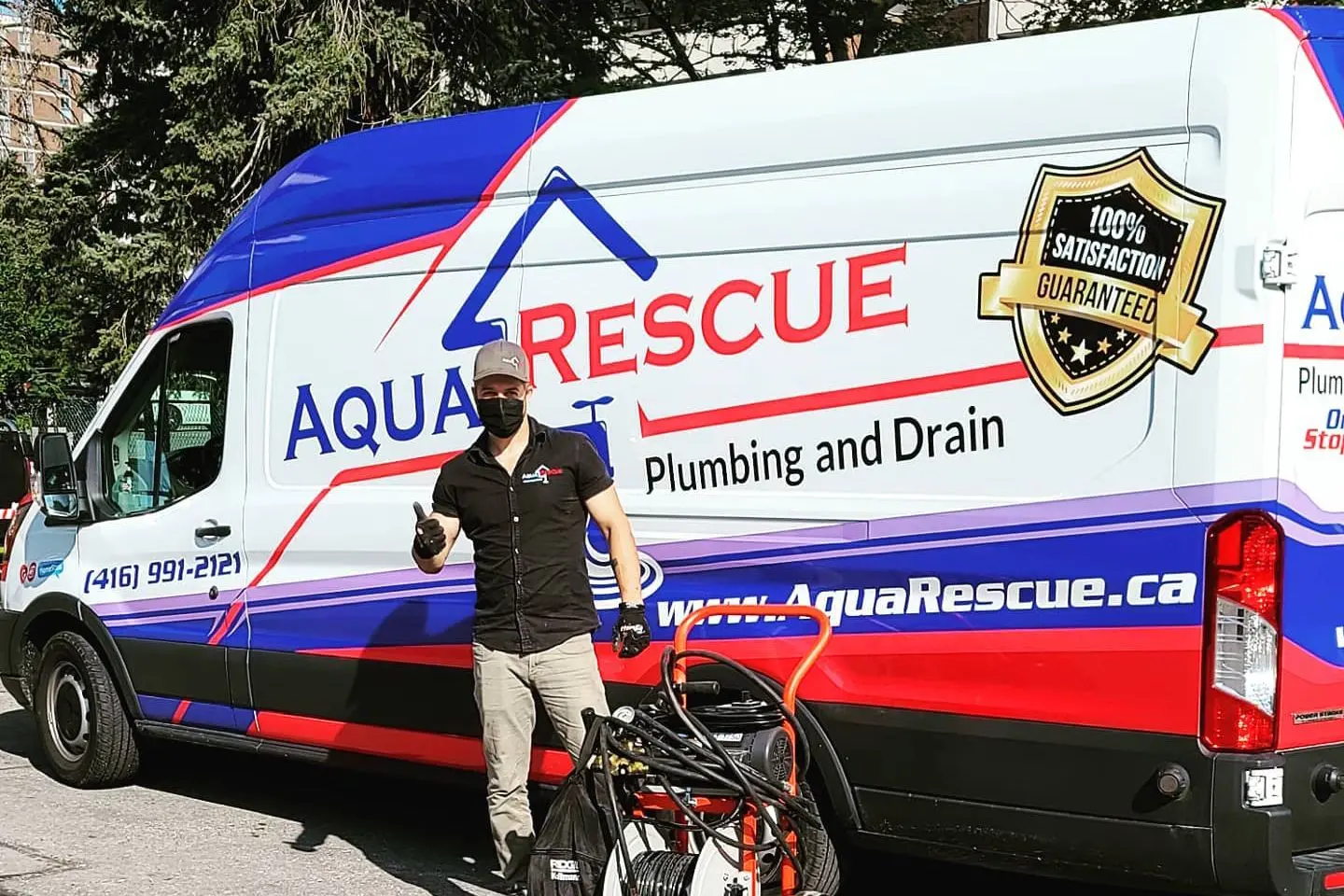 A person stands in front of an Aqua Rescue Plumbing and Drain service van, which is white with blue and red accents, displaying company branding and a “100% Satisfaction Guaranteed” badge.