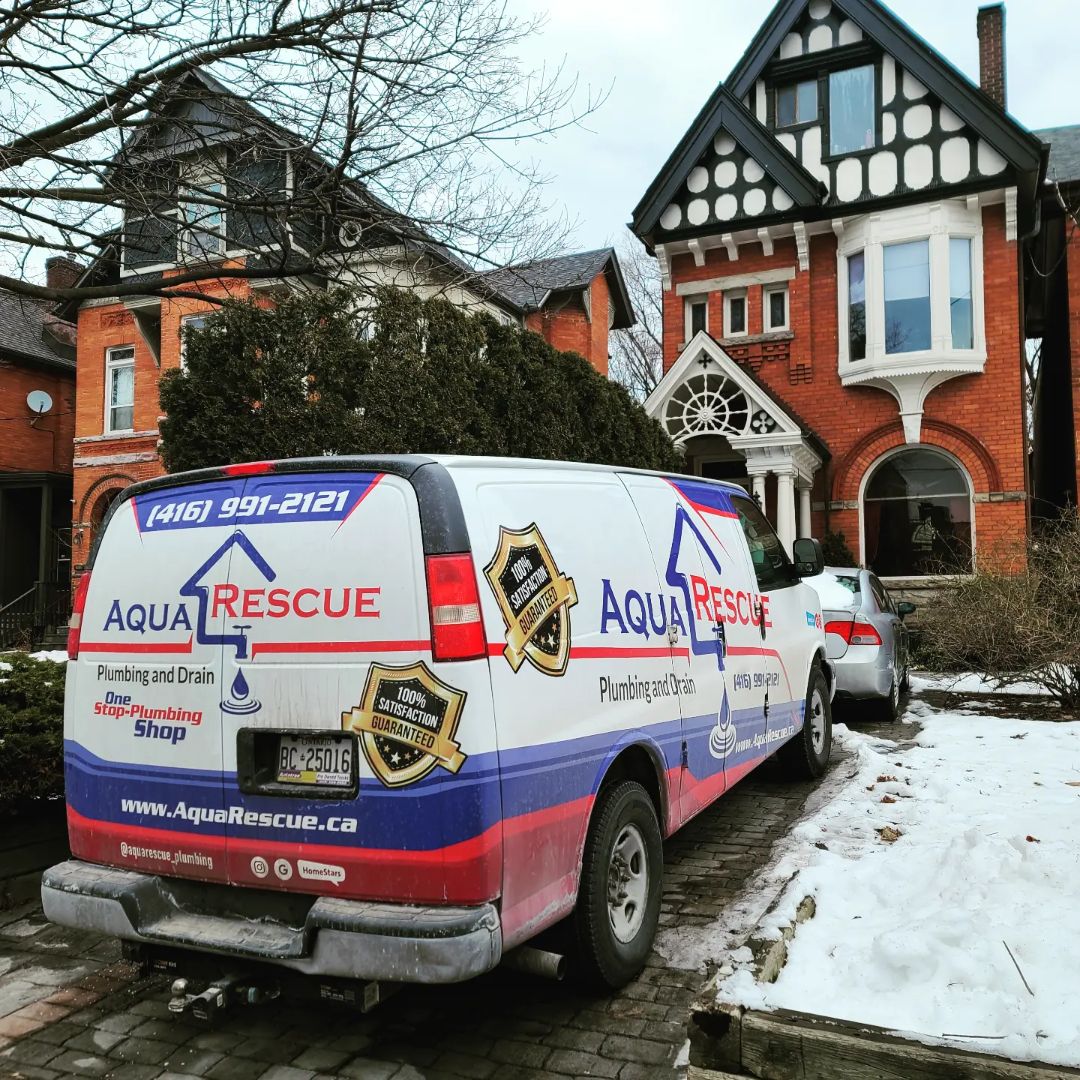 Aqua Rescue plumbing service van parked in front of a large red-brick Victorian-style house on a snowy residential street.